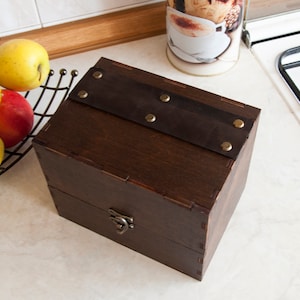 May include: A dark brown wooden box with a leather strap and brass accents. The box has a hinged lid and a brass latch.