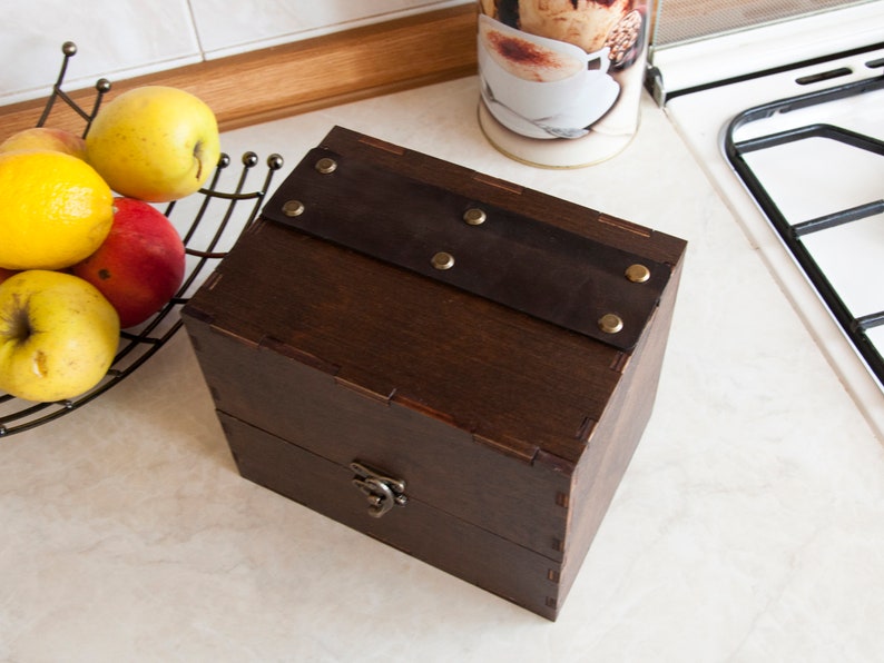 May include: A dark brown wooden box with a leather strap and brass accents. The box has a hinged lid and a brass latch.