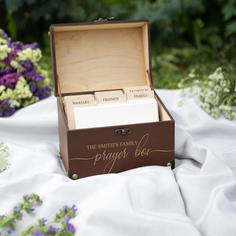 May include: A brown wooden box with a hinged lid and a brass latch. The box is labeled "The Smith's Family Prayer Box" and has five compartments labeled "Salvation/Family", "Friends", "Warfare", "Health", and "Other".