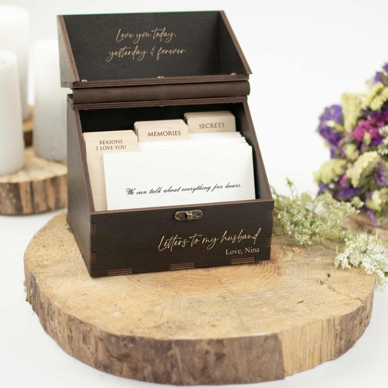 May include: A wooden box with a hinged lid, engraved with the words "Love you today, yesterday & forever". The box is open, revealing a set of cards with categories like "Reasons I Love You", "Memories", and "Secrets". The box is labeled "Letters to my husband, Love, Nina".