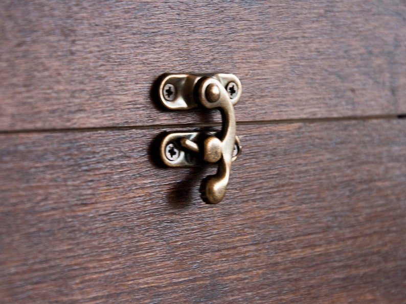Peut inclure: Gros plan sur une bo&icirc;te en bois avec un loquet de couleur laiton. Le grain du bois est visible et le loquet est fix&eacute; avec de petites vis. La bo&icirc;te semble &ecirc;tre en bois brun fonc&eacute;.