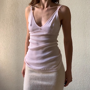 Op de afbeelding: Een wit geribbeld tanktop met dunne bandjes en een delicate kantversiering. Het tanktop heeft een ronde hals en een aansluitende pasvorm.