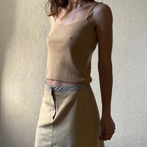 以下が含まれることがあります： 薄いストラップが付いたタン色のキャミソールトップと、お揃いのスカート。トップはVネックで、フィットしたシルエットです。スカートも同様のタン色で、ボタン留めです。この衣装は、柔らかく軽い生地で作られています。