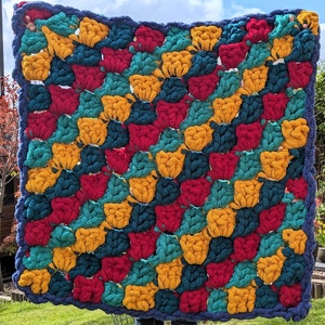 May include: A colourful crocheted blanket with a geometric pattern in shades of red, yellow, teal, and blue.