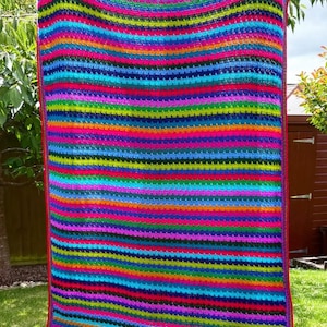 May include: A vibrant, handmade crochet blanket with horizontal stripes in a rainbow of colors, including red, pink, orange, yellow, green, blue, and purple. The blanket has a red border and is displayed outdoors.