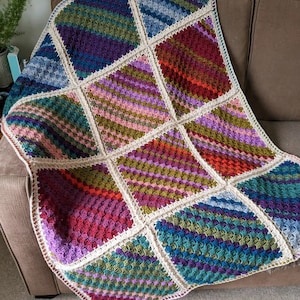 May include: A colourful crocheted throw blanket with a variety of textures and patterns. The blanket is made up of squares in shades of purple, green, blue, red, and pink.