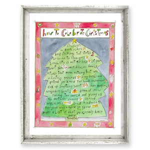 May include: A framed watercolor print with the text "how To Celebrate Christmas". The artwork features a Christmas tree shape filled with handwritten text and festive decorations in red, green, and yellow. The frame is white.