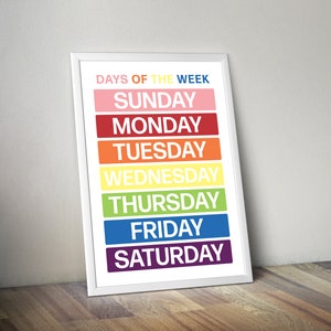 May include: A white framed poster with the text "Days of the Week" in black. The days of the week are listed in a rainbow color scheme, with Sunday in pink, Monday in red, Tuesday in orange, Wednesday in yellow, Thursday in green, Friday in blue, and Saturday in purple.