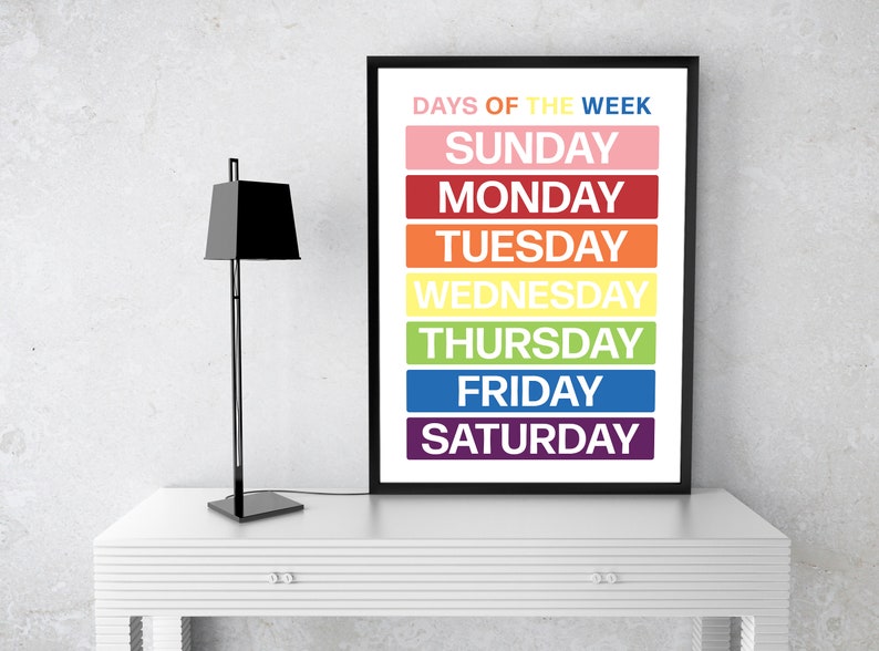 May include: A black framed poster with the text "Days of the Week" in white. The days of the week are listed in a column, each in a different color: Sunday (pink), Monday (red), Tuesday (orange), Wednesday (yellow), Thursday (green), Friday (blue), and Saturday (purple).