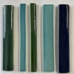 May include: Five ceramic tile samples in different colors. The tiles are arranged from left to right: dark green, light blue, dark green, light blue, and dark blue.
