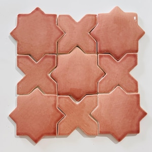 May include: A collection of nine ceramic tiles arranged in a square grid pattern. The tiles alternate between an eight-pointed star shape and a four-pointed cross shape, all featuring a glossy, solid dusty rose pink finish with smooth edges.