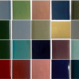 May include: A grid of twenty square ceramic tiles featuring a diverse palette of glossy and matte finishes. The colors include shades of blue, green, pink, yellow, gray, red, brown, and deep purple, arranged in a four-by-five rectangular layout.