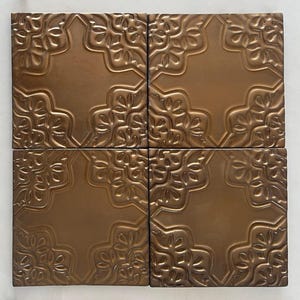 May include: Four square bronze tiles with an embossed floral pattern. The tiles are arranged in a grid pattern.