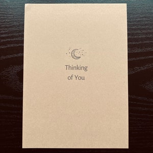 May include: A simple card with a crescent moon and stars design. The card says "Thinking of You".