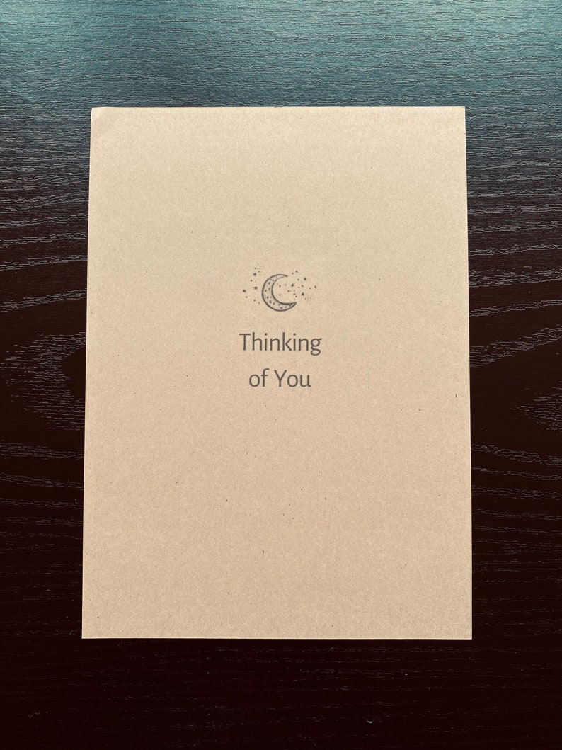 May include: A simple card with a crescent moon and stars design. The card says "Thinking of You".