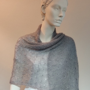 Può includere: Un scialle di maglia grigia con un delicato motivo traforato. Lo scialle è drappeggiato sulle spalle di un manichino.