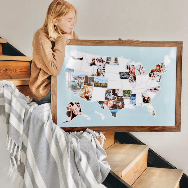 May include: A framed map of the United States with photos of different locations in each state. The map is on a light blue background and has a brown wooden frame.