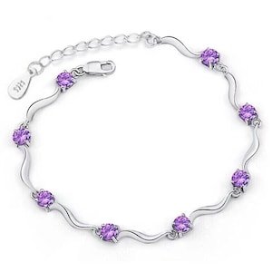 May include: A silver bracelet with a wavy design and purple gemstones. The bracelet has a lobster clasp closure.
