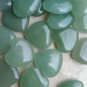 May include: A collection of polished, heart-shaped green stones. The stones have a smooth, glossy surface and vary slightly in shade, from light to medium green. The hearts are arranged closely together, filling the frame.