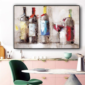 May include: Abstract painting of wine bottles and a glass of red wine. The bottles have colorful wax seals and labels. The artwork is displayed in a kitchen setting with pink cabinets, a green chair, and a marble table.