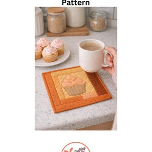 May include: A square, quilted mug mat with a cupcake design. The mat features a patchwork design in shades of orange and brown. A white mug with a beverage sits on the mat. The text "Cupcake Mug Mat Pattern" is at the top.