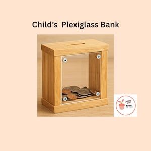 May include: A wooden child's bank with a clear plexiglass front, filled with coins. The bank has a slot on top for inserting money. The text "Child's Plexiglass Bank" is above the bank.