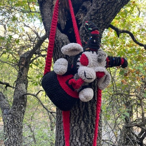 May include: A black and red crocheted bag with a gray and red crocheted plush toy attached to the strap. The bag and toy are hanging from a tree branch.