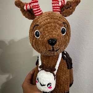 May include: A brown crocheted reindeer with red and white striped antlers and a white crocheted bag with a smiling face.
