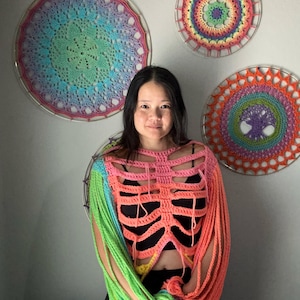 May include: A colorful crochet top with a skeleton design. The top is made with a variety of bright colors, including pink, green, yellow, and blue. The sleeves are long and flowy, and the top is cropped.
