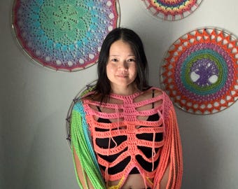 Puede incluir: Un top de crochet colorido con un diseño de esqueleto. El top está hecho con una variedad de colores brillantes, incluyendo rosa, verde, amarillo y azul. Las mangas son largas y fluidas, y el top es corto.