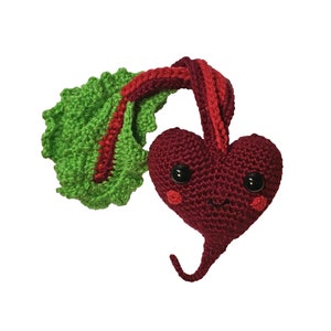May include: A handmade crochet beet with a smiling face, black button eyes, and rosy cheeks. The beet is a deep burgundy color, with a green and red leafy top. The whimsical design is crafted with soft yarn.