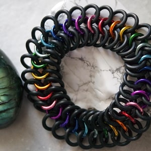 May include: A rainbow colored chainmail bracelet made of black and metallic rings.