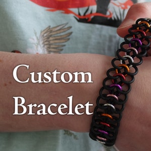 Könnte beinhalten: Ein individuelles Armband aus schwarzen, orangen, silbernen, rosa und violetten Ringen. Das Armband befindet sich am Handgelenk einer Person und der Text "Custom Bracelet" ist auf dem Bild sichtbar.