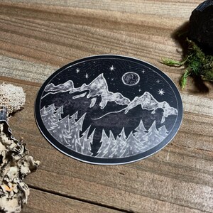 May include: Black and white sticker with a moon, stars, mountains, and trees. The sticker is round and has a white outline.