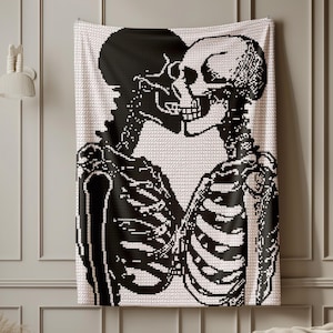 May include: Black and white tapestry featuring a skeletal couple in an embrace. The artwork depicts two skeletons kissing, set against a light pink background. The tapestry is a decorative piece, suitable for wall decor.