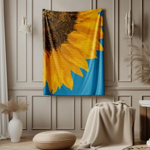 Op de afbeelding: Een wandkleed met een close-up van een gele zonnebloem op een blauwe achtergrond.