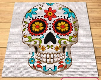 Puede incluir: Una calavera de azúcar colorida con diseños florales y ojos negros. La calavera es blanca con detalles rojos, amarillos, verdes y azules.