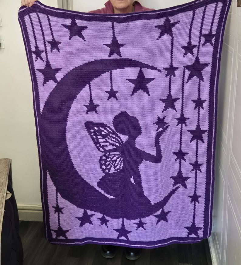 May include: A rectangular crochet blanket featuring a dark purple silhouette of a fairy with wings sitting on a crescent moon against a light purple background. The design includes numerous dark purple stars hanging from vertical lines.