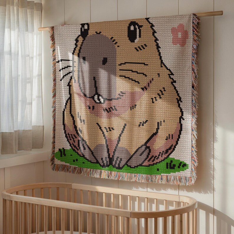 Puede incluir: Un tapiz de pared tejido con un capibara de estilo de dibujos animados con un patr&oacute;n de pelaje marr&oacute;n y beige. El capibara est&aacute; sentado en un parche de hierba verde con una flor rosa en el fondo.