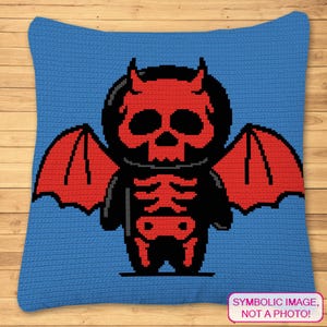 Könnte beinhalten: Ein blaues gehäkeltes Kissen mit einem roten und schwarzen Pixelbild eines Teufels mit Flügeln. Der Text "SYMBOLISCHES BILD, KEIN FOTO!" befindet sich am unteren Rand des Kissens.