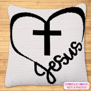 May include: White crochet pillow with a black heart and cross design. The word "Jesus" is written in a script font within the heart. The pillow has a textured appearance and is displayed on a wooden surface.