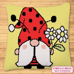 May include: A crocheted pillow featuring a gnome with a ladybug hat, holding a bouquet of white flowers. The gnome is wearing a red and black striped shirt and black pants. The pillow is yellow with a white border.