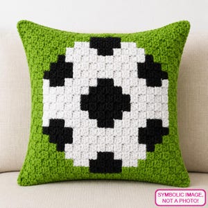 May include: A square, green crocheted pillow with a black and white soccer ball design in the center. The pillow is made of a textured yarn and is displayed on a neutral-colored surface. The text "SYMBOLIC IMAGE, NOT A PHOTO!" is in the bottom right corner.