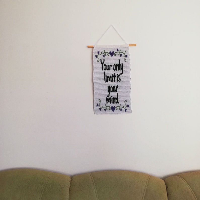 Pu&ograve; includere: Arazzo da parete bianco con una citazione ricamata in nero che recita "Your only limit is your mind." L'arazzo &egrave; decorato con piccoli cuori viola e viti verdi.