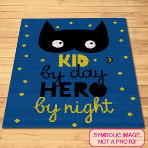 Pode incluir: Cobertor de crochê azul com uma máscara de super-herói preta e branca e o texto "Kid by day Hero by night".