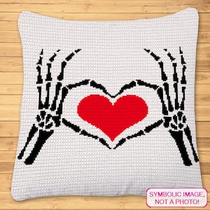 May include: A white crocheted pillow with two black skeletal hands forming a heart shape around a red heart. The pillow has the text "SYMBOLIC IMAGE, NOT A PHOTO!" in a pink box at the bottom.