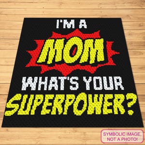 Pode incluir: Tapete quadrado preto com o texto "I'M A MOM WHAT'S YOUR SUPERPOWER?" em fonte pixelizada branca e amarela. A palavra "MOM" está em fonte amarela com um fundo vermelho em forma de explosão. O tapete está sobre uma superfície de madeira.