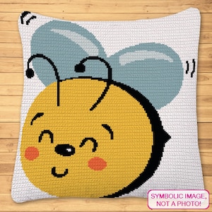 May include: A crocheted pillow with a yellow bee face with black eyes and a black nose. The bee has two blue wings with white accents. The pillow has a white background with the text "SYMBOLIC IMAGE, NOT A PHOTO!" at the bottom.