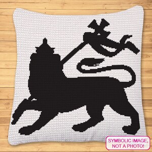 Puede incluir: Una almohada blanca de crochet con una silueta negra de un león sosteniendo una bandera. El león está de pie sobre sus cuatro patas y tiene una corona en la cabeza. La bandera es un diseño estilizado con una forma curva. El texto "IMAGEN SIMBÓLICA, ¡NO UNA FOTO!" está impreso en una etiqueta blanca en la esquina inferior derecha de la almohada.