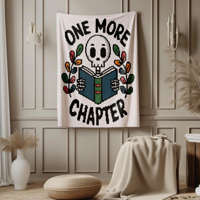 May include: A white crochet wall hanging featuring a pixelated skull reading a blue and green book. The text "ONE MORE CHAPTER" is stitched in black above and below the skull. Two colorful leafy branches frame the central design.